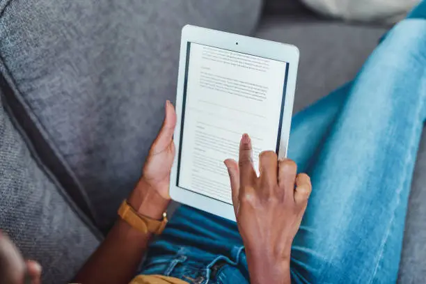 A person relaxing on a couch, holding a tablet and reading a document or ebook, with their finger poised to scroll the screen. ebooks benefits 2